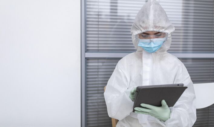 冠状病毒穿防护服的人看着平板电脑防护服预防生物危害