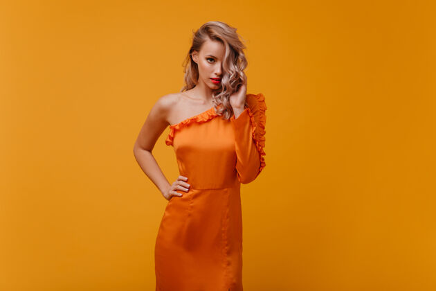 放松穿着橙色连衣裙的时髦女人朝前看波浪发性感服饰