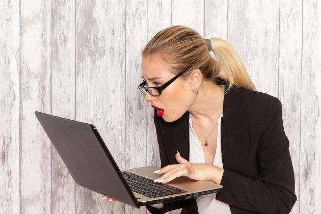 视图正面图年轻女商人穿着严苛的衣服黑色夹克在白色办公桌上用笔记本电脑办公女商人衣服便携式电脑女