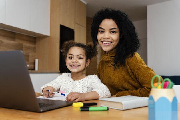小笑脸少女用平板电脑在网上学校帮助小妹妹的正面图青少年笔记本电脑孩子