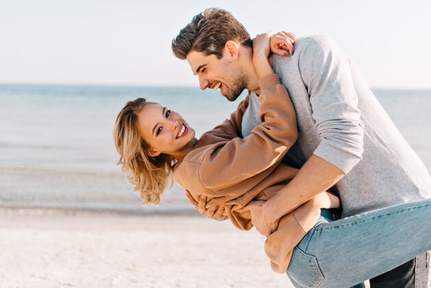 旅行一位金发短发的女士在沙滩上拥抱着丈夫在海边 一位幽默的男士和女友跳舞的户外写真度假自然蜜月