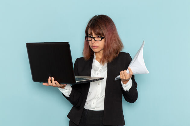 正面正面图：穿着正装的女上班族 使用笔记本电脑 拿着纸放在浅蓝色的表面上套装使用女