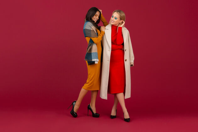 夹克两位穿着秋冬时装礼服和外套的时尚女性在红墙上孤零零地摆着姿势魅力时尚配饰