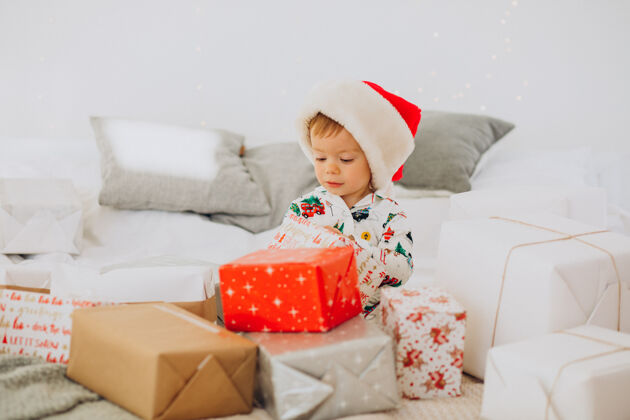 灯戴圣诞帽的可爱男孩在圣诞节打开礼物小圣诞乐趣