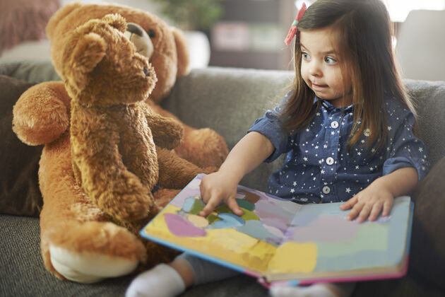 天真小女孩和她的泰迪熊一起看书休闲服装玩具泰迪熊