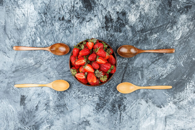顶部把一碗草莓和木勺平放在深蓝色大理石表面水平浆果甜点特写