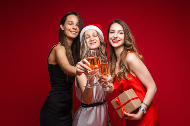 年轻人快乐的年轻女性朋友们带着礼物和香槟一起庆祝节日派对上的红色背景 复制空间庆祝青年庆祝