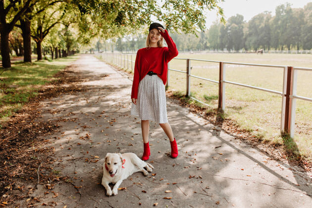 明亮漂亮的年轻女子和她可爱的狗在户外玩得很开心穿着红色套头衫和时髦鞋子的金发女郎在秋季公园玩得很开心金发户外时尚