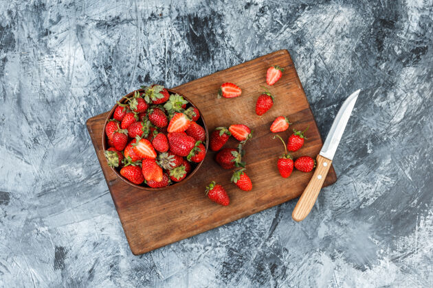 多汁一碗草莓和一把刀放在深蓝色大理石背景的木制砧板上平铺木板桌子铺设