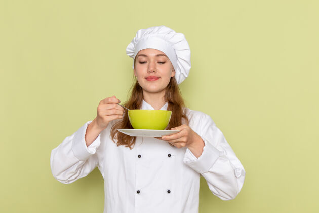 晚餐身穿白色厨师服的女厨师手持绿色盘子 绿色桌子上放着菜厨房烹饪美食女厨师的正视图前面帽子女厨师