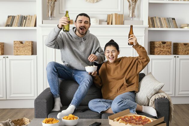 室内夫妻俩在室内喝啤酒吃零食一起看电视室内