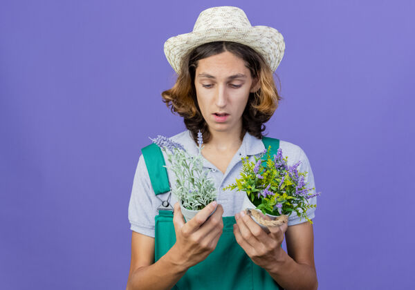 穿著年輕的園丁 穿著連體衣 戴著帽子 手里拿著盆栽植物男人連身衣站著