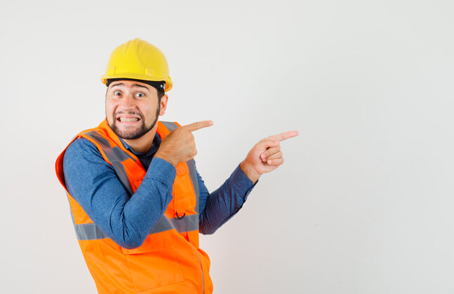 建筑工人年轻的建设者穿着衬衫 背心 头盔指着侧面 神情好奇 前视图工人建筑专业