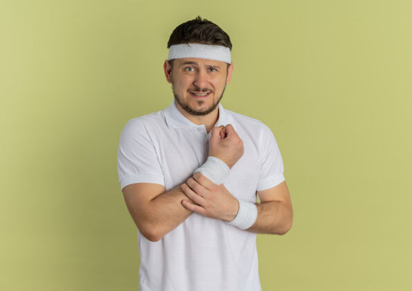 运动装身穿白衬衫 头箍朝前看的年轻健身男子站在橄榄墙外 手碰到手腕感到疼痛运动运动人