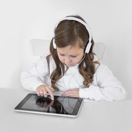 年轻人小女孩用带耳机的平板电脑消遣年轻人娱乐