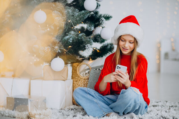 网上商店圣诞节 在圣诞树旁打电话的女孩灯节日帽子
