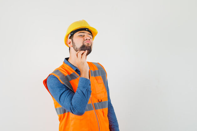 刮擦年轻的建筑工人穿着衬衫 背心 头盔刮胡子 看上去很优雅 前视图头盔工作年轻