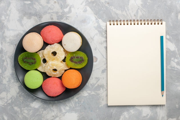 新鲜顶视图彩色小蛋糕和干菠萝戒指在浅白色的桌子上水果干的顶部