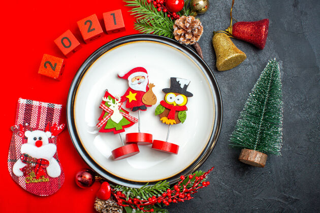 容器新年背景的顶视图 带有餐盘装饰配件杉木树枝和数字圣诞袜 放在黑色桌子上圣诞树旁的红色餐巾上餐巾风景树枝