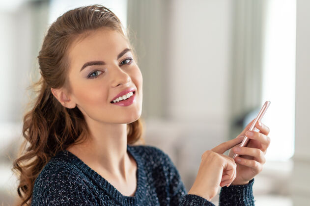 电话快乐的年轻女人在家里看着她的智能手机女人在她的智能手机上输入信息交谈微笑白种人
