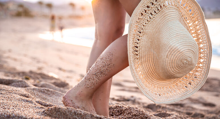 腿身体的一部分日落时分一个戴着帽子站在海滩上的女人的脚沙滩休息帽子