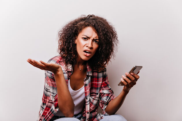 表情不幸的黑人女孩拿着智能手机在白色暴躁的非洲妇女在红衬衫智能手机非洲休闲