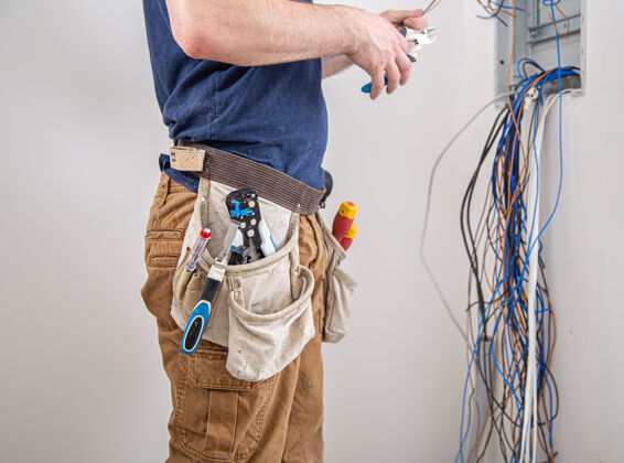 修理工电工建筑工人在工作时 检查工业配电盘机身电线中的电缆连接专业人员穿着工作服 手持电工工具技师设备故障排除