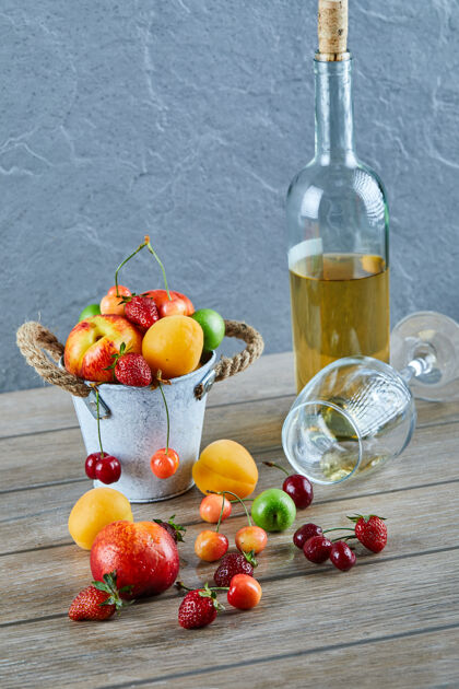 天然木桌上有一桶夏天的新鲜水果 一瓶白葡萄酒和空杯子油桃景观酸橙
