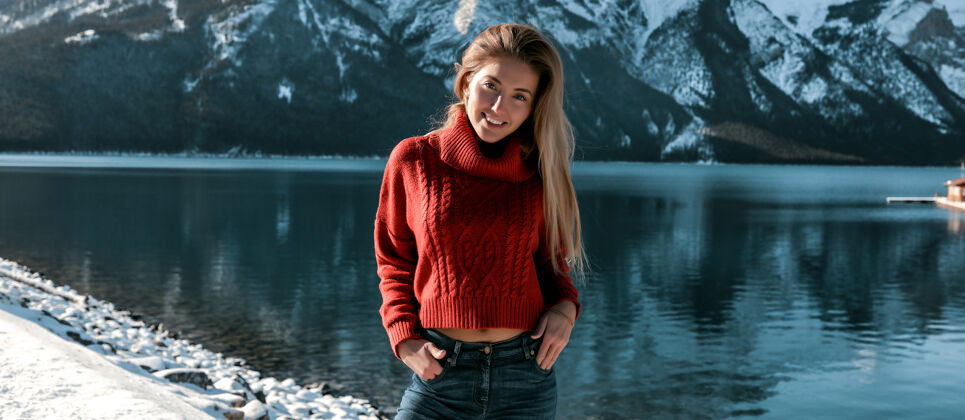 旅游美丽的女士站在雪域岸边的深湖和惊人的山景快乐的女孩在超大毛衣和牛仔裤没有化妆和长金发发型蓝天男人徒步旅行天空