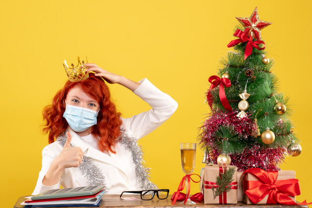 新正面图：戴着面具的女医生在圣诞礼物上戴着黄色的皇冠坐医生背景