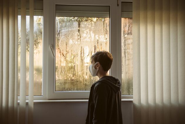 Ncov戴着口罩的男孩站在窗户旁边疾病健康检疫