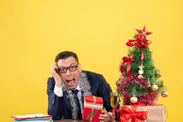圣诞节圣诞树旁的桌子上 拿着礼物和黄色礼物的欢欣男子的正面图举行西装肖像