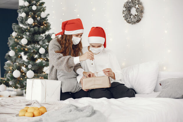 装饰为圣诞节做准备的人冠状病毒主题妈妈和儿子玩穿白毛衣的男孩十二月花环家庭