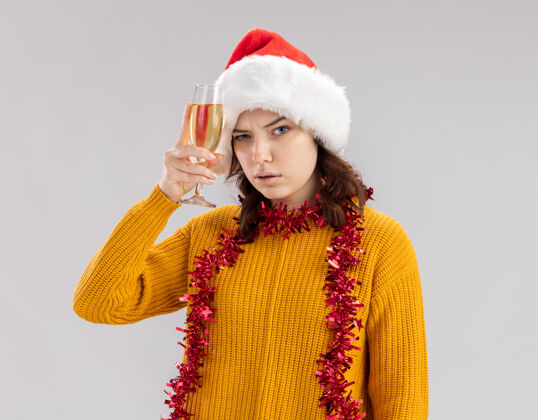 圣诞快乐自信的年轻斯拉夫女孩 戴着圣诞帽 脖子上戴着花环 手里拿着一杯香槟 背景是白色的 有复制空间花环年轻自信
