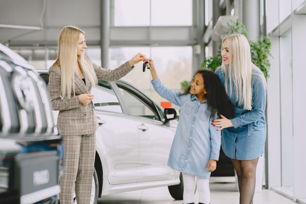 客户一家人在汽车沙龙里买车的女人和妈妈在一起的非洲小女孩和客户在一起的经理商店零售女儿