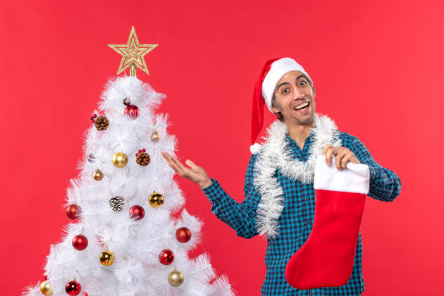 庆祝兴奋骄傲快乐的年轻人 戴着圣诞老人帽 穿着蓝色条纹衬衫 手里拿着圣诞袜子年轻人衬衫自豪