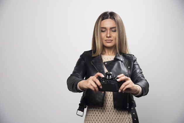 女人穿着黑色皮夹克的年轻女士严肃而专业地用相机拍照设备相机模型