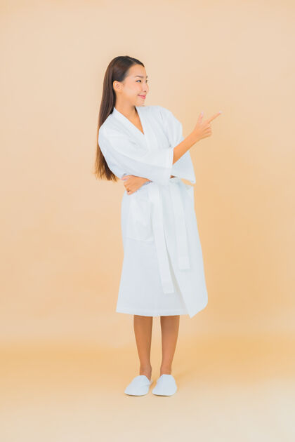 面霜肖像美丽的亚洲年轻女子穿着米色的微笑浴袍面部清洁面部