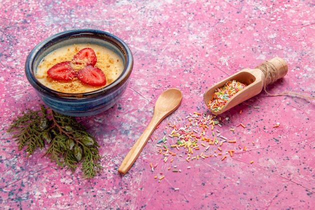 餐具正面图美味的奶油甜点和淡粉色墙壁上的红色草莓片甜点冰淇淋甜浆果木制勺子浆果奶油