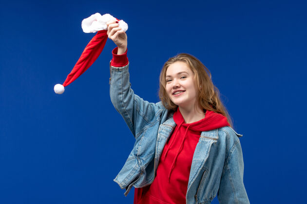 秘书前视图年轻女性手持蓝色背景上的红色圣诞帽 喜怒哀乐举行歌手情绪