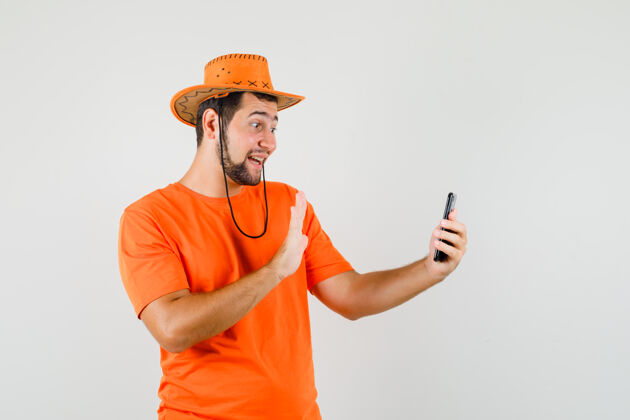 模特年轻人一边挥手一边自拍 身穿橙色t恤 戴着帽子 看上去很开心男人时尚现代