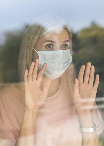 Ncov大流行期间 戴着医用口罩的妇女在家触摸窗户的正面图隔离妇女窗户