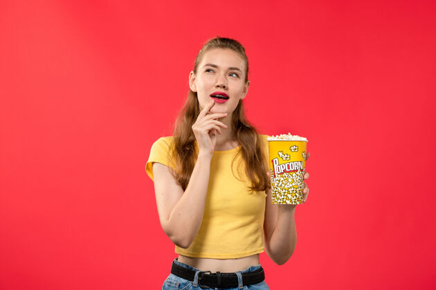 年轻女性正面图年轻女性在电影院拿着爆米花包 思考着红墙电影院的女性趣味电影思考成人女性