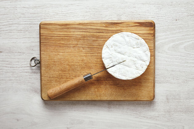圆形老白木桌上的砧板上 一把木柄的反刀夹着卡门伯特奶酪营养切割美味