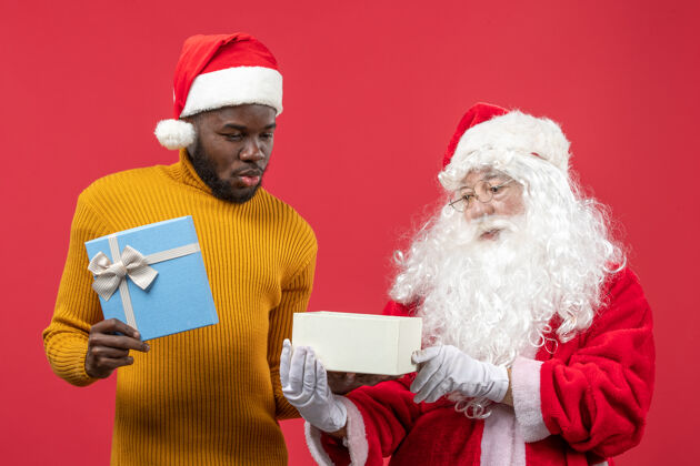 圣诞红墙上的圣诞老人和拿着礼物的年轻人的正视图快乐举行男性