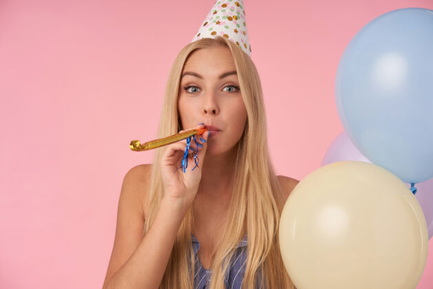 年轻室内照片的积极长发金发女性庆祝节日与党的服装 与粉红色背景上的五彩气球摆姿势人 娱乐和节日属性漂亮室内节日