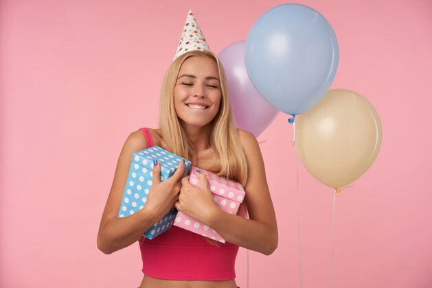庆祝这张照片拍摄的是一位快乐的长发女士 她留着随意的发型 用五彩气球庆祝生日 在收到很棒的礼物时表现出快乐的反应 隔离在粉色背景上情感女性欢快