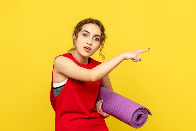 快乐黄色墙壁上拿着紫色地毯的年轻女子的正视图模特瑜伽运动
