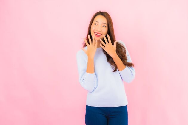 手势美丽的亚洲年轻女子在粉红色的隔离墙上微笑日本人庆祝化妆