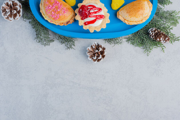美味小面包 一个纸杯蛋糕和果冻糖果放在一个蓝色的盘子里 上面装饰着松叶和圆锥形的大理石表面甜点美味面包